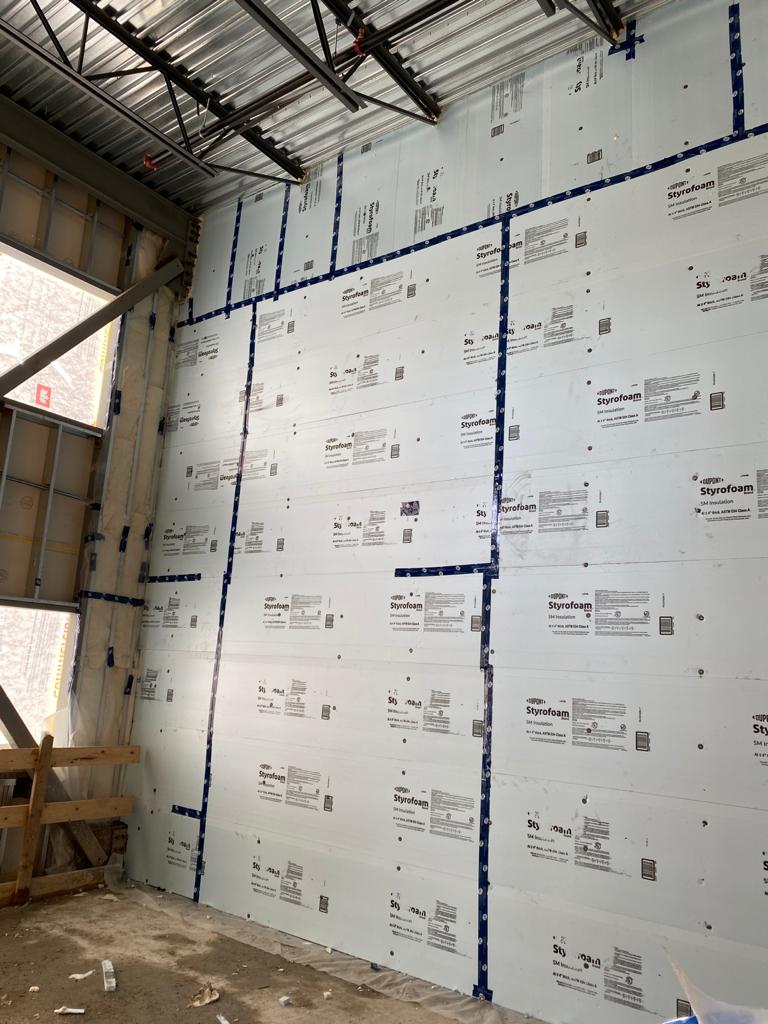 White Styrofoam rigid insulation boards installed on interior wall with blue tape seams