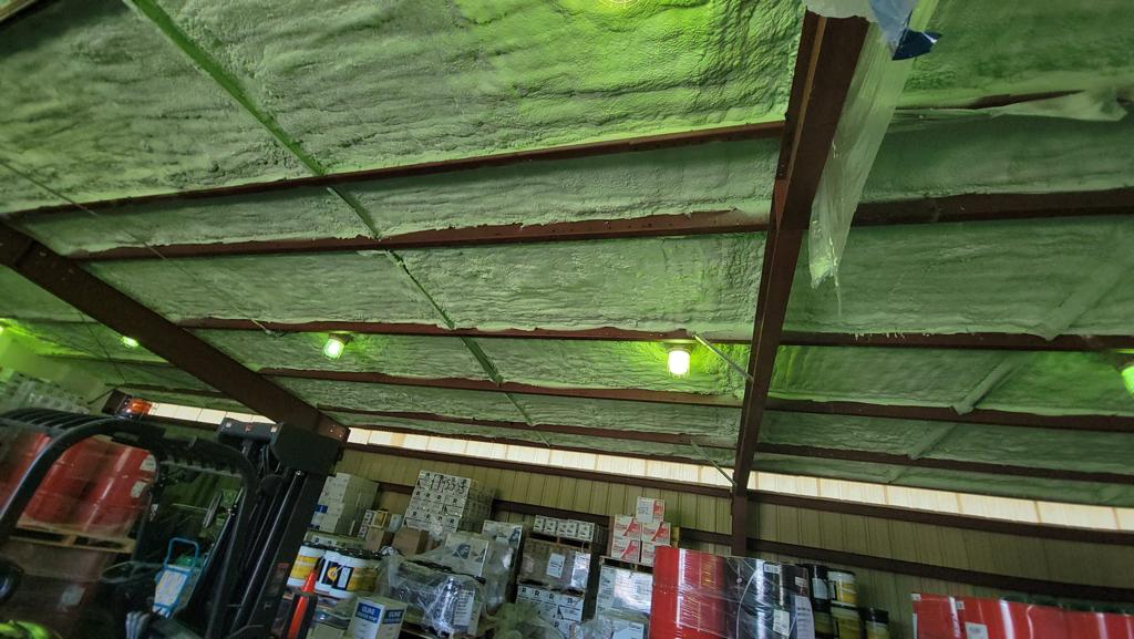 Professional spray foam insulation application showing green foam on ceiling beams in warehouse